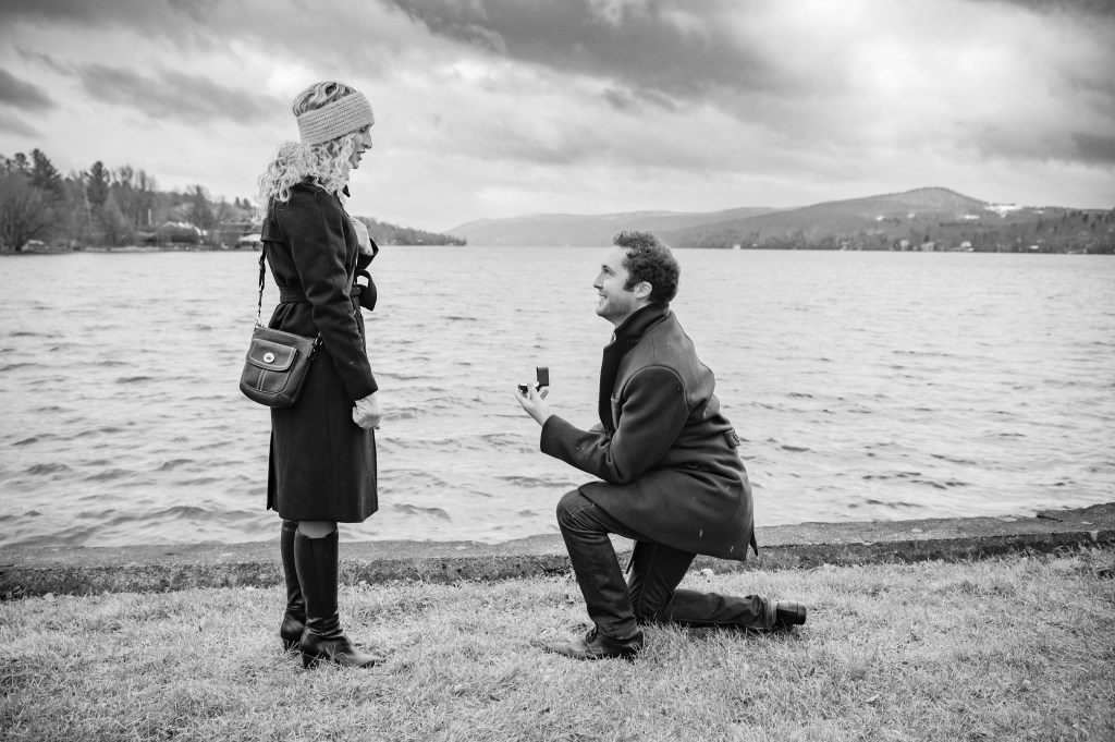 Un homme propose à une femme au bord d'un lac, sous un ciel nuageux, dans une ambiance romantique.
