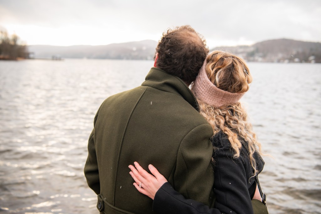 Un couple se tenant par les bras près d'un lac, avec des paysages naturels en arrière-plan.