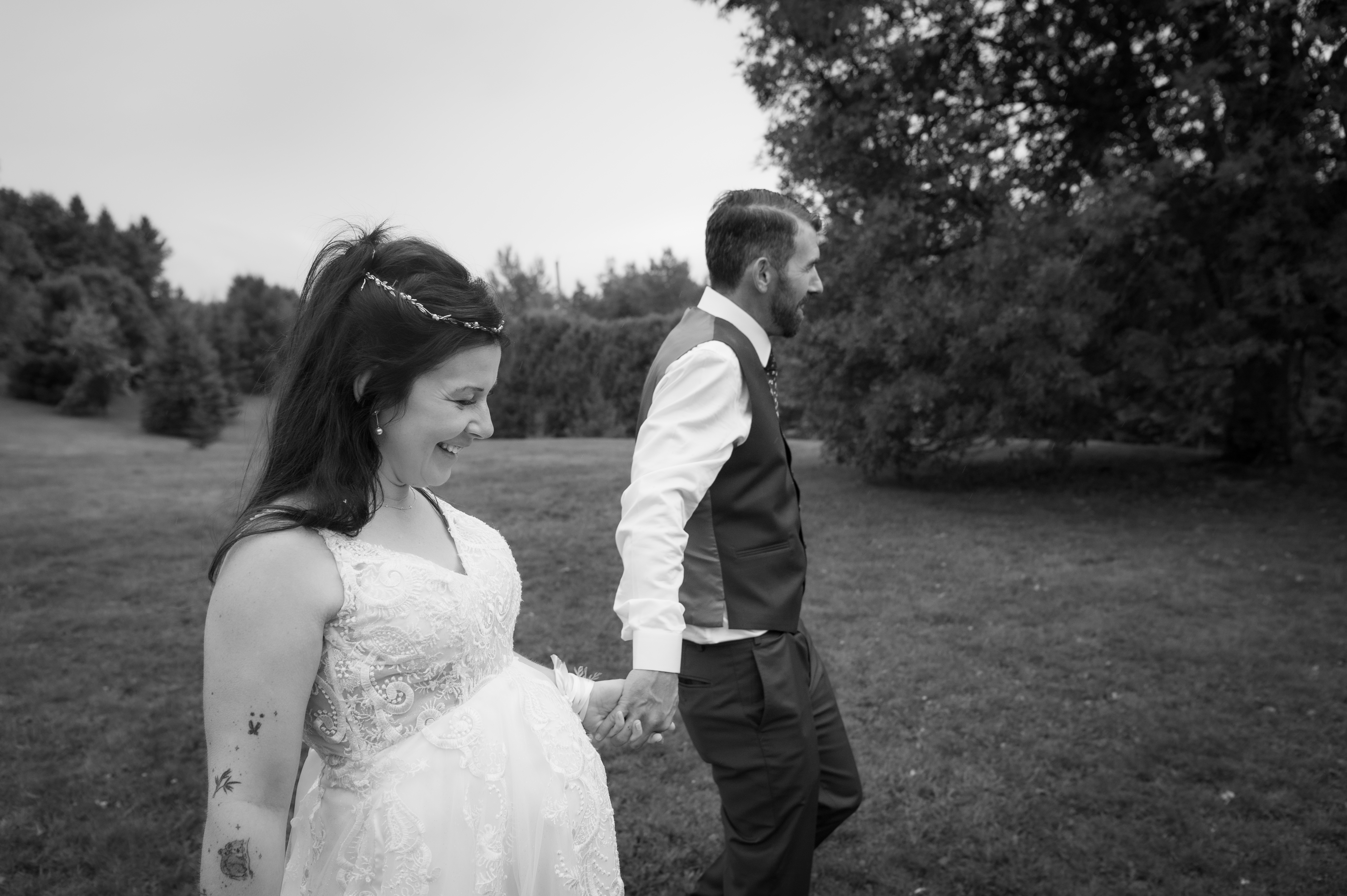 Une mariée souriante en robe blanche marche main dans la main avec un homme en costume, dans au Estrimont à Orford.