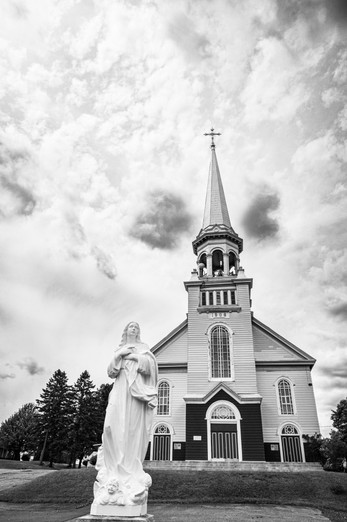 Église avec une statue de la Vierge Marie au premier plan, en noir et blanc.