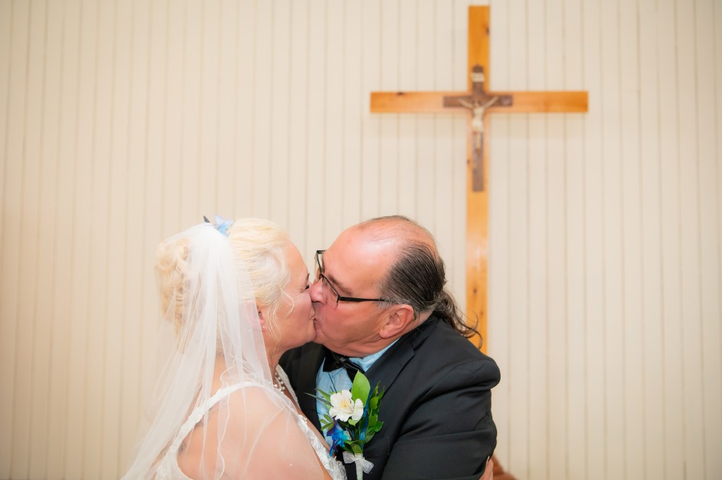 Un couple marié s'embrassant devant une croix en bois.
