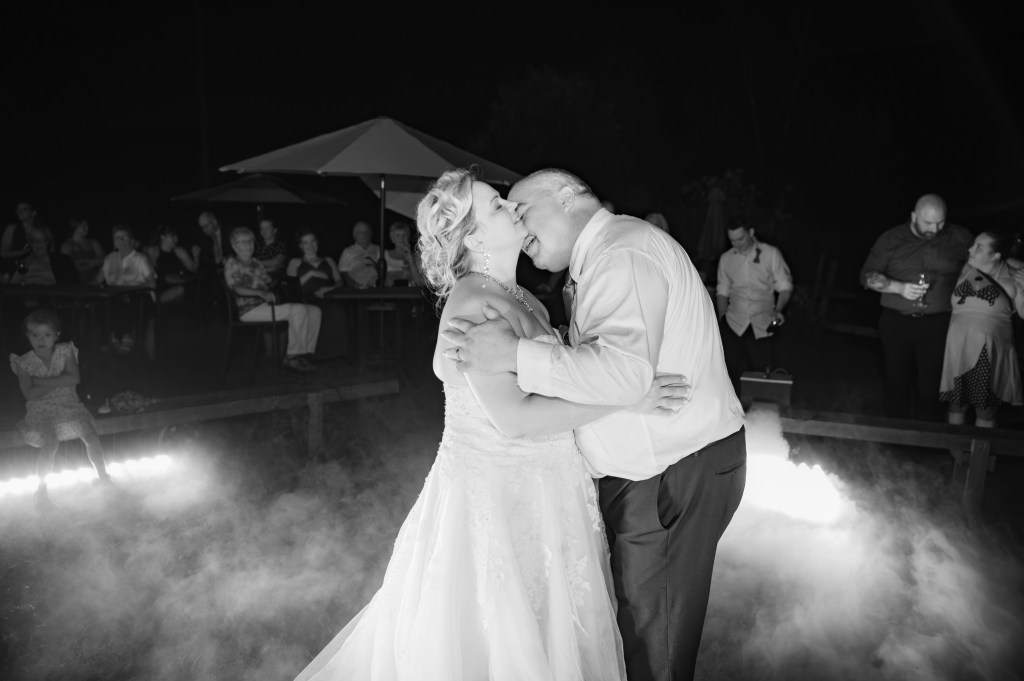 Un couple s'embrassant sur la piste de danse lors de leur mariage, entouré d'invités, dans une ambiance nocturne avec des lumières tamisées.