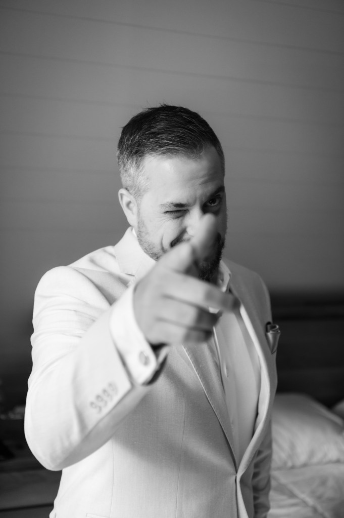 Homme en costume clair, winking et pointant du doigt vers l'objectif.