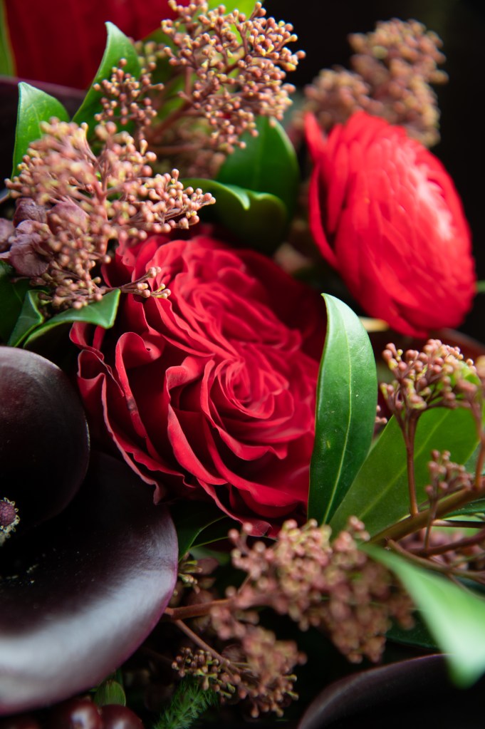 Un bouquet de fleurs comprenant des roses rouges, des feuilles vertes et des brindilles fleuries.