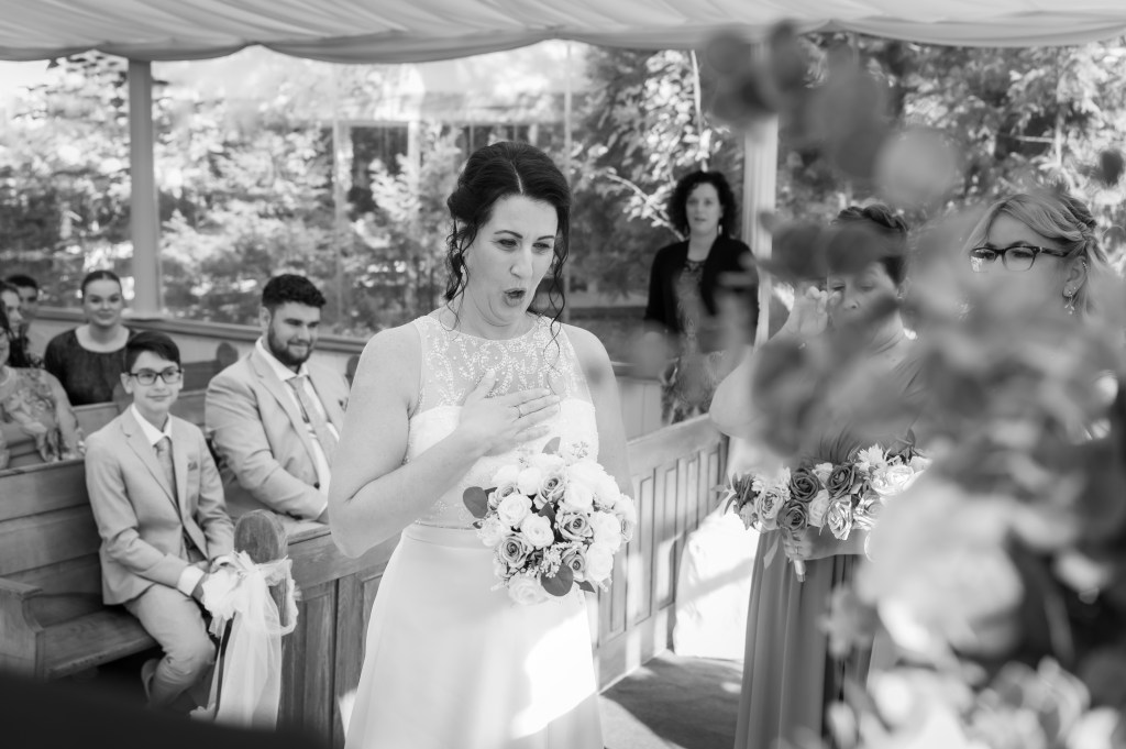 Une mariée émue avec un bouquet de roses, entourée de ses demoiselles d'honneur et des invités lors de la cérémonie de mariage.
