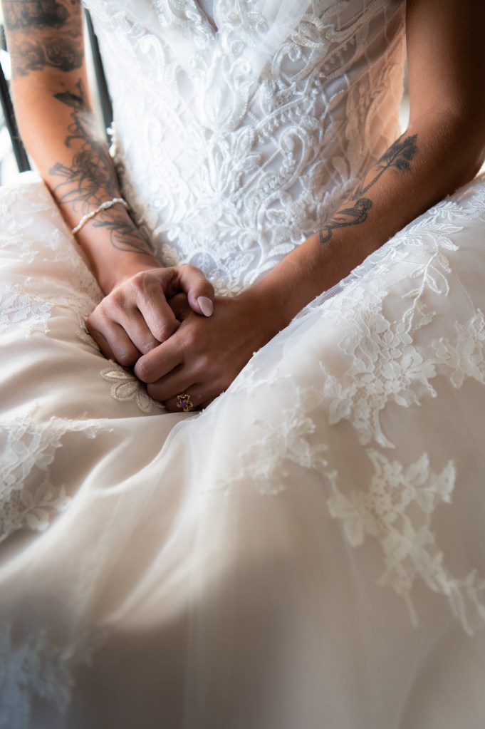 Détail d'une mariée portant une robe de mariage avec des broderies et des tatouages visibles sur les bras.