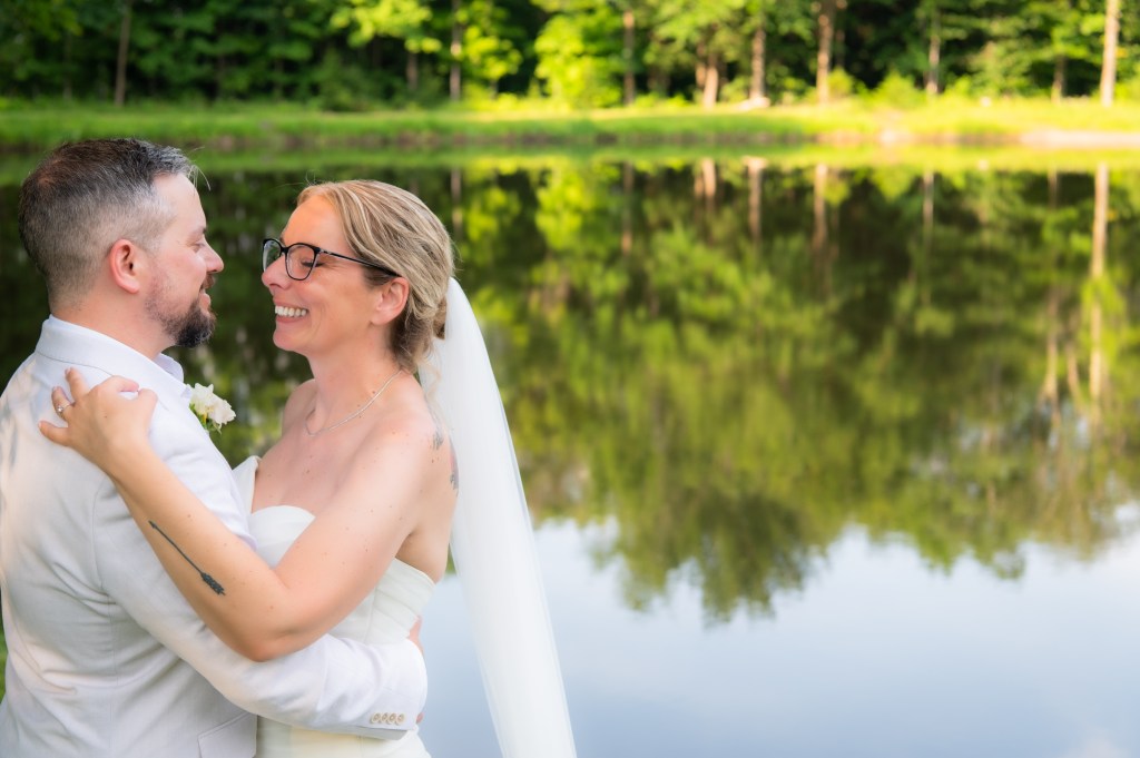 Un couple de mariés se regardant affectueusement au bord d'un étang, entouré d'une verdure luxuriante.
