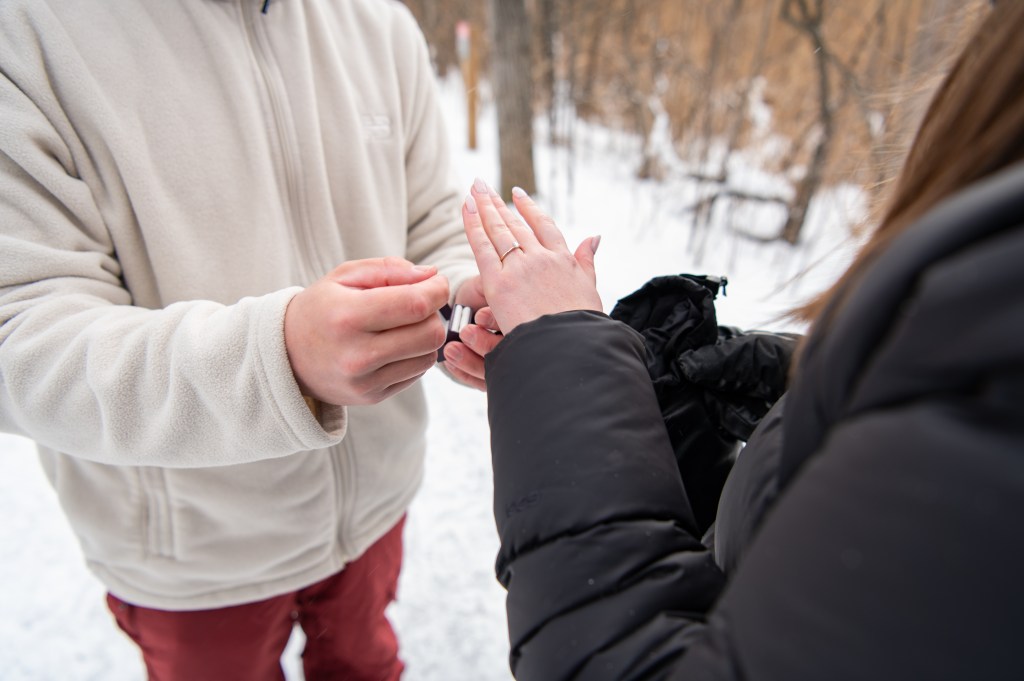 Une personne en train de mettre une bague à l'annulaire d'une femme dans un environnement enneigé.